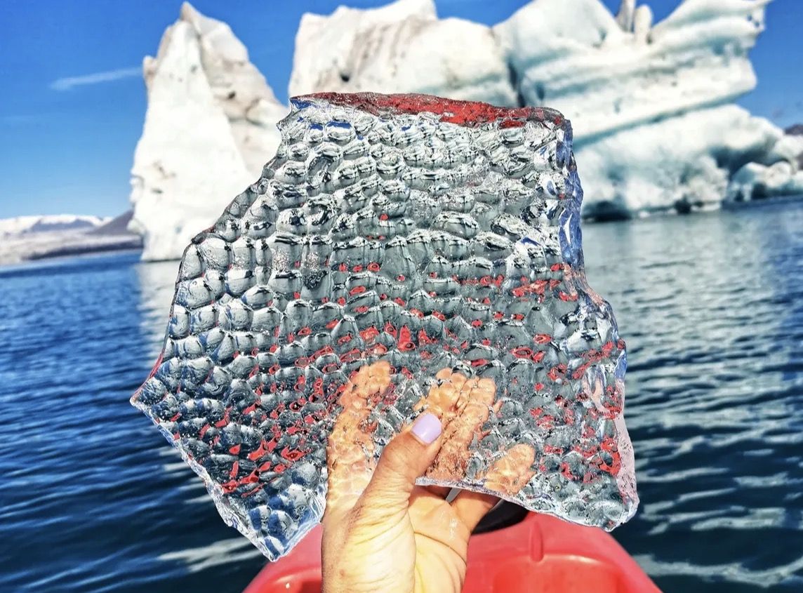 A seal resting on a small iceberg on the calm waters of Jökulsárlón while visitors photograph from the shore