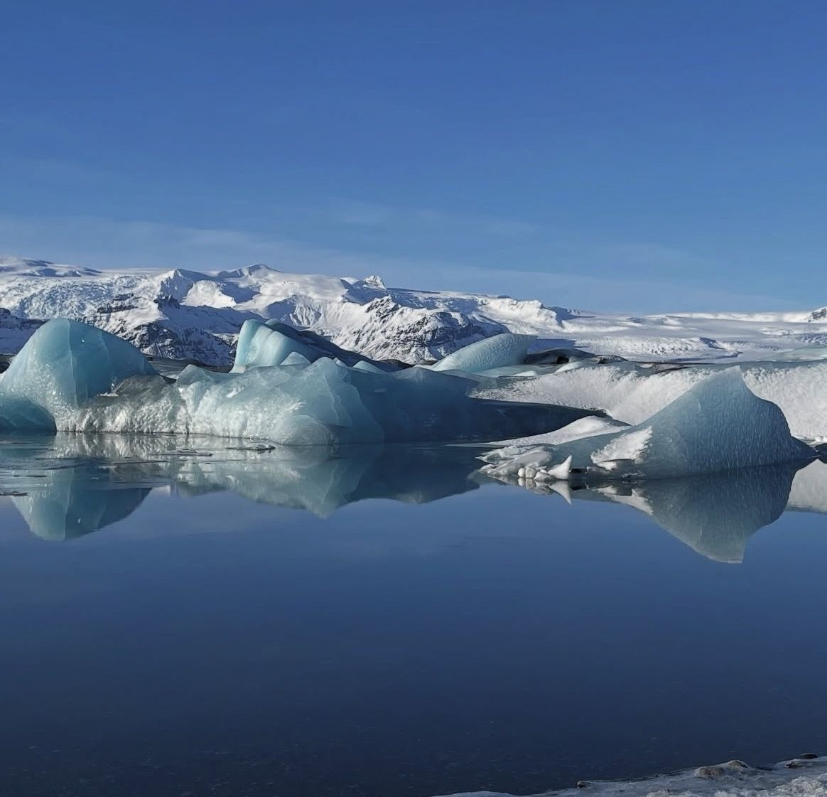 A hiker in full waterproof gear standing at the edge of Jökulsárlón in winter with icebergs behind them